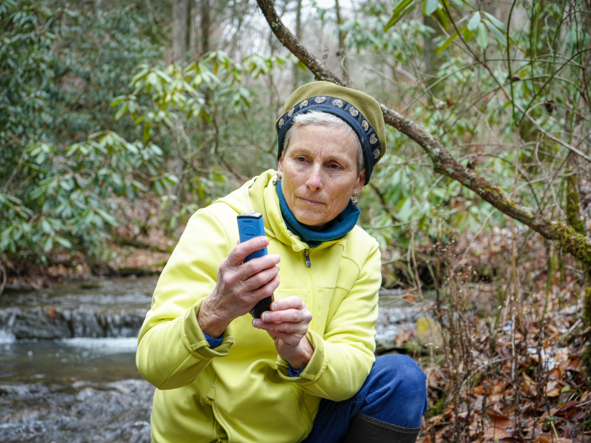 Mimi Kibler squats in a stream to take measurements of the stream water.