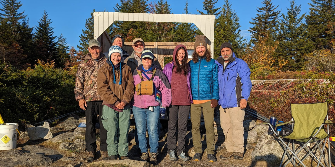 A group of people stand in front of the bird banding station at Dolly Sods with trees in the background